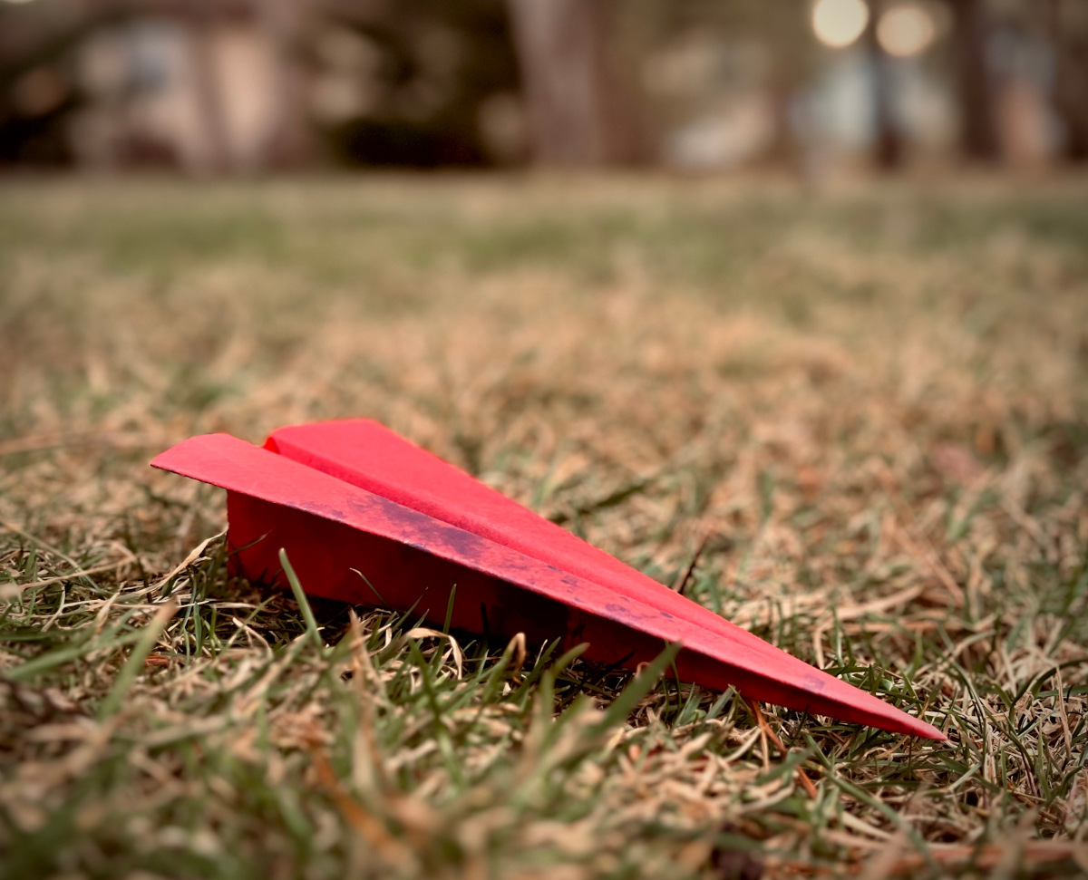A red paper airplane on grass.